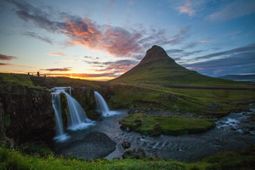Photograph of sun setting behind mountain in Iceland with waterfalls in foreground.